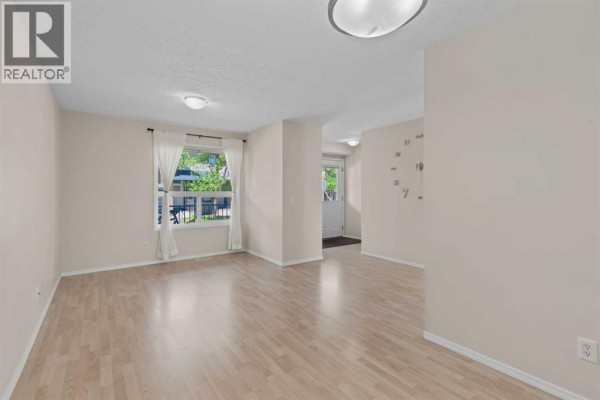 Living room with light wood floors, beige walls, white curtains, and a view of the outdoors. - 34 Eversyde Common Sw, Calgary