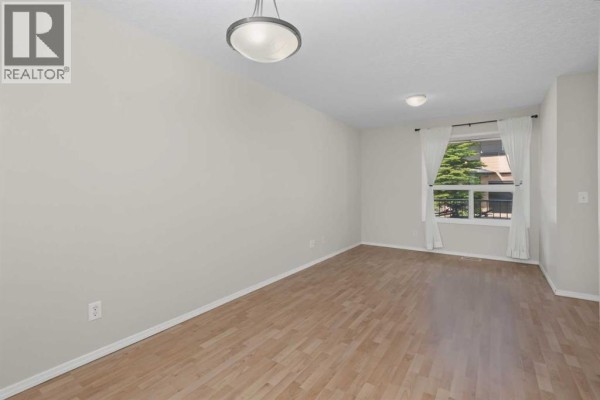 Dining area with light wood floors, beige walls, white curtains, and a window overlooking greenery. - 34 Eversyde Common Sw, Calgary