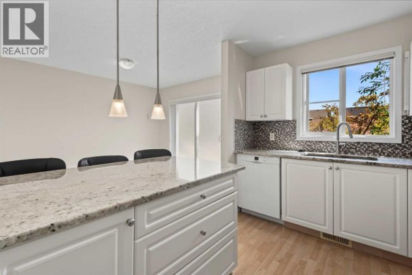 Kitchen with white cabinets, granite countertops, mosaic tile backsplash, and a large island with pendant lights. - 34 Eversyde Common Sw, Calgary