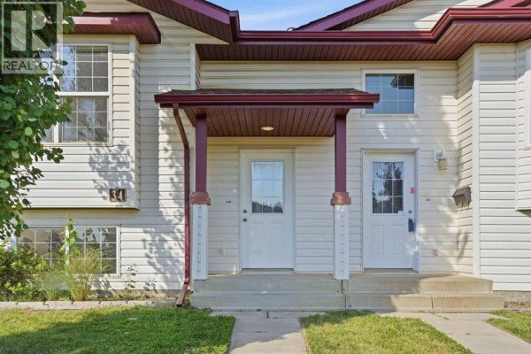Close-up of the duplex entrance with two white doors, burgundy trim, and concrete steps. - 34 Keen Crescent, Red Deer