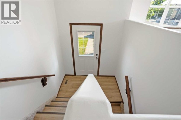 Interior view looking down a staircase with white walls, wooden handrails, and a door at the bottom. - 34 Keen Crescent, Red Deer