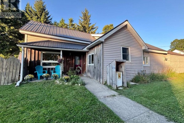 Front door and porch detail with wood siding, two teal chairs, and potted plants. - 34 Main Street, Arran Elderslie