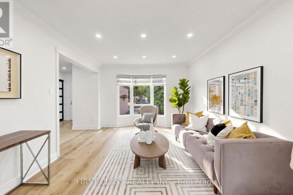 Living room with light wood floors, a grey sofa, and a bay window. - 34 Mayberry Court, Brampton
