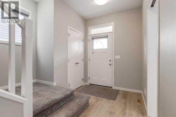 Interior entryway with carpeted stairs, white doors, and light wood-look flooring. - 34 Midtown  Sw, Airdrie
