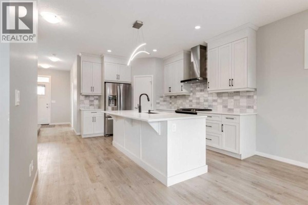 Open concept kitchen and living area with white cabinets and light wood flooring. - 34 Midtown  Sw, Airdrie