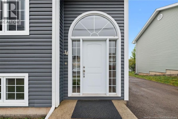 Close-up of the white front door with arched window, surrounded by grey siding and white trim. - 34 Monique Street, Moncton