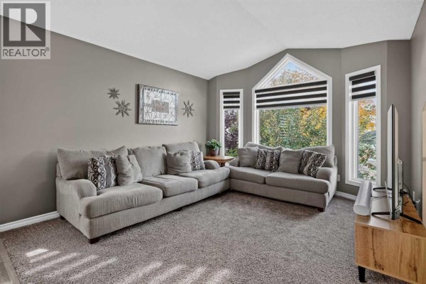 Living room with a sectional sofa, large windows, and grey walls with decorative wall art. - 34 Mt Aberdeen Link Se, Calgary