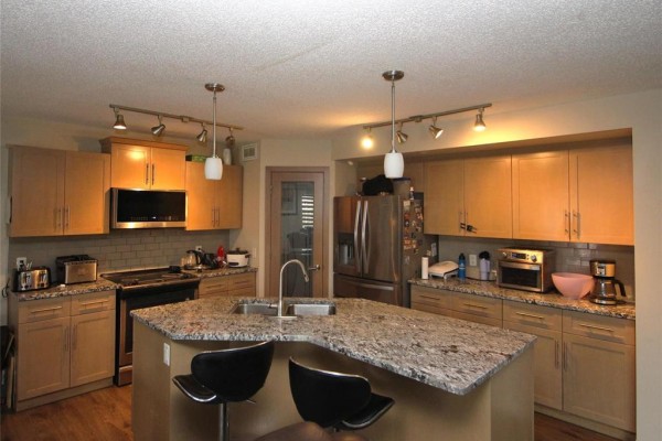 Bright kitchen with light wood cabinets, granite countertops, an island with stools, and stainless steel appliances. - 34 Red Wing Cove, Winnipeg