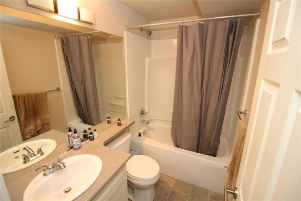 A full bathroom with a double vanity, toilet, and bathtub with a gray shower curtain. - 34 Red Wing Cove, Winnipeg