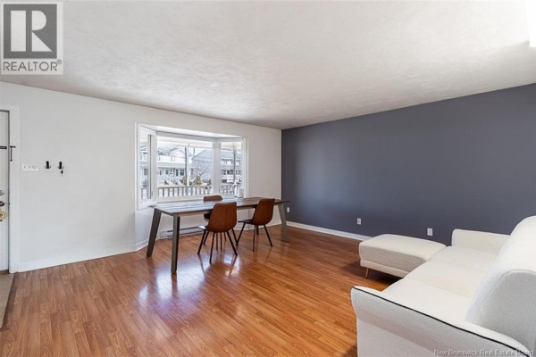 Living and dining area with a bay window, wood table, and white sofa. - 34 Rennick Road, Moncton