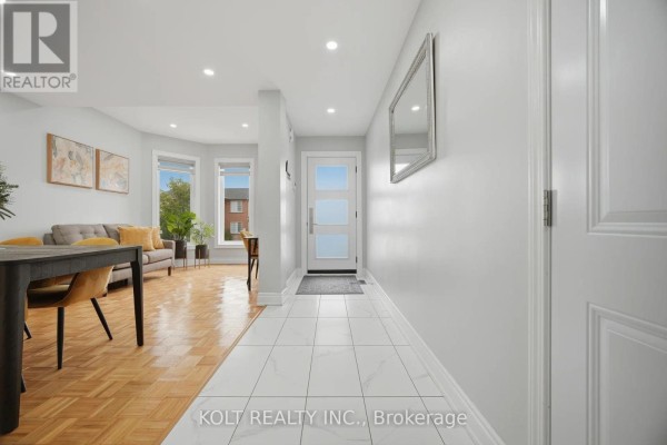 Interior hallway with white tiled floor leading to a glass front door and living area. - 34 Saddleback Square, Brampton