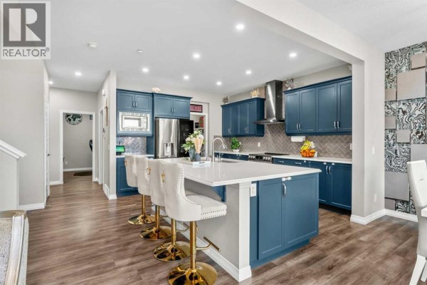 View of a spacious kitchen featuring dark blue cabinetry, a stainless steel refrigerator, and a quartz-topped island. - 34 Seton Road Se, Calgary