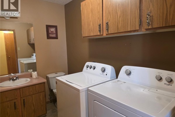 Laundry room with a white washing machine and dryer, wood cabinets, and laundry baskets. - 34 Stanley Street, Creelman