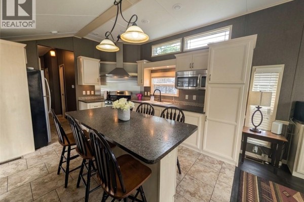 A spacious mobile home kitchen with a large island, white cabinets, stainless steel appliances, and pendant lights. - 34 Temagami Trail, Wasaga Beach