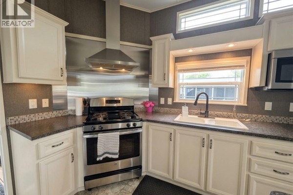 Close-up of a mobile home kitchen sink, faucet, white cabinets, and stainless steel gas range with a vent hood. - 34 Temagami Trail, Wasaga Beach
