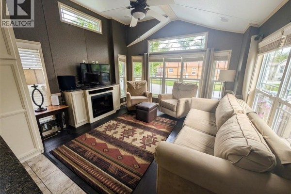 Living room in a mobile home with a large sectional sofa, armchair, fireplace, television, and large windows. - 34 Temagami Trail, Wasaga Beach