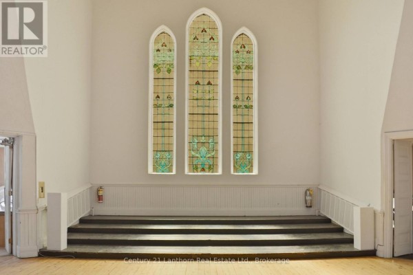 Stage area with a raised platform, three arched stained glass windows, and white wainscoting. - 34 Victoria Avenue, Belleville