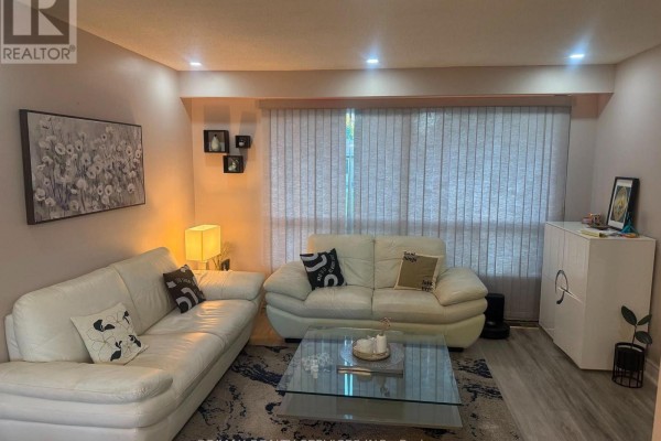 Living room with two white leather sofas, a glass coffee table, and vertical blinds. - 34 Watson Crescent, Brampton