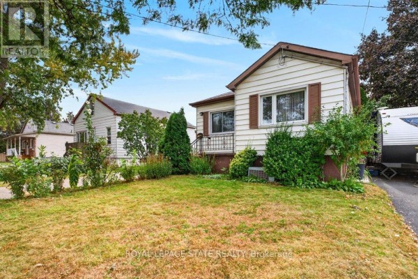 Side view of a white bungalow with brown trim, showing a small porch and lush landscaping. - 340 Barton Street, Hamilton