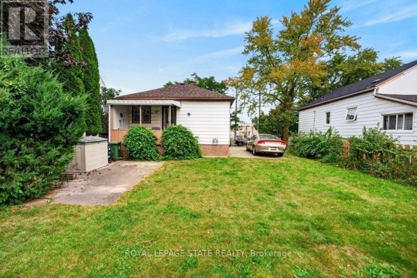 View of the side and back of the house with a grassy yard, mature trees, and parked car. - 340 Barton Street, Hamilton
