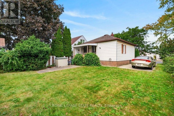 Exterior view of the bungalow showing a white siding and brown roof with a well-maintained lawn. - 340 Barton Street, Hamilton