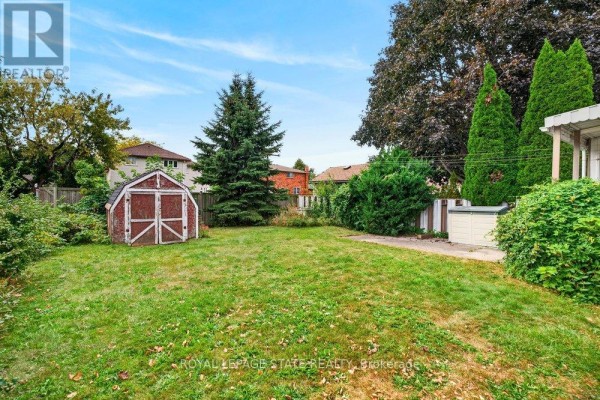 Backyard with a green lawn, mature trees, a small red shed, and privacy fencing. - 340 Barton Street, Hamilton