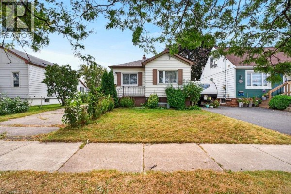 Front view of a detached bungalow with white siding and brown trim, centered on a green lawn. - 340 Barton Street, Stoney Creek