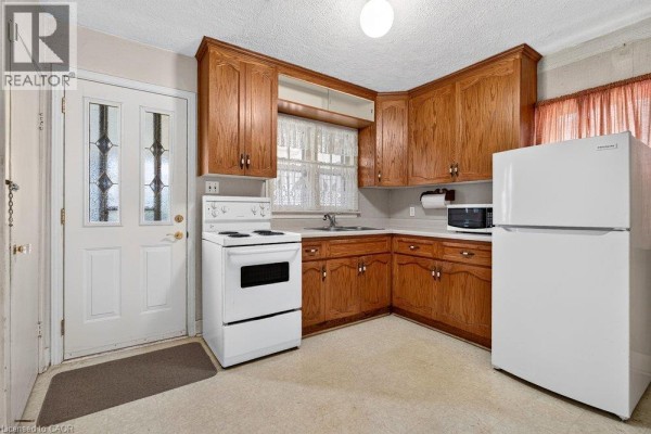 Kitchen with oak cabinets, white appliances, white countertops, and linoleum flooring. - 340 Barton Street, Stoney Creek