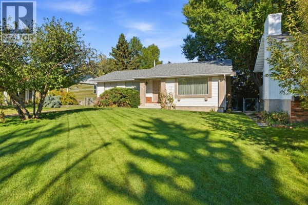 Side view of the bungalow's beige siding, white chimney, and green lawn. - 340 Canniff Place Sw, Calgary
