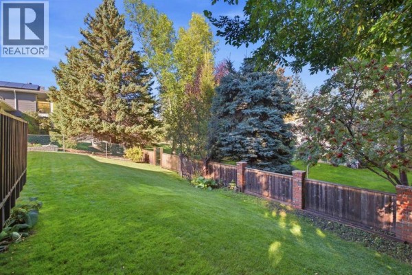 Backyard view with a wooden fence, green grass, and the rear of the house. - 340 Canniff Place Sw, Calgary