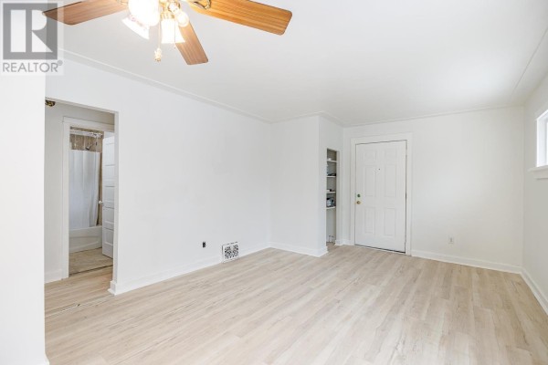 Living room with white walls, light wood-look flooring, a door to a bathroom, and a white front door. - 340 Wellington St, Sault Ste  Marie