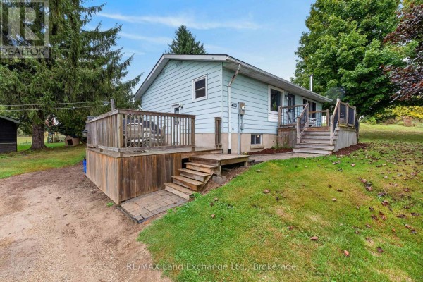 Side view of a light blue sided house with a large wooden deck and stairs, surrounded by green grass and trees. - 3400 Highway 9 Highway, Brockton