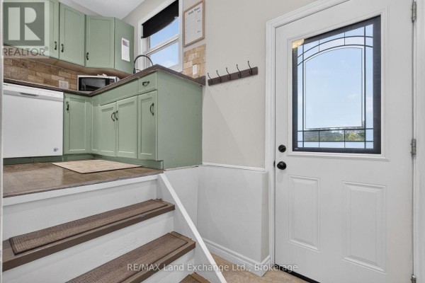 View from entryway of a kitchen with green cabinets, tiled backsplash, and stairs leading down to a lower level. - 3400 Highway 9 Highway, Brockton