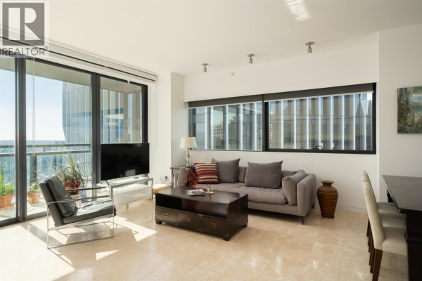 Living room area with grey sofa, coffee table, and large windows overlooking the city. - 3403 838 W Hastings Street, Vancouver