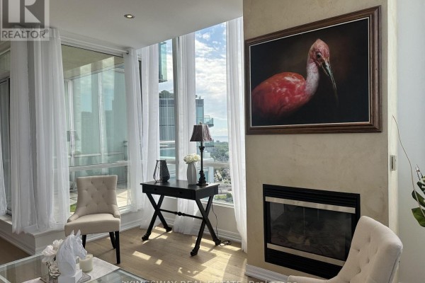Living room corner with a gas fireplace, framed artwork, and upholstered chairs. - 3404 - 220 Burnhamthorpe Road W, Mississauga