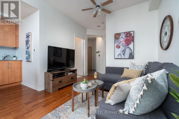 Living room and kitchen with wood cabinets, stainless steel appliances, and view of city buildings. - 3404 - 55 Bremner Boulevard, Toronto