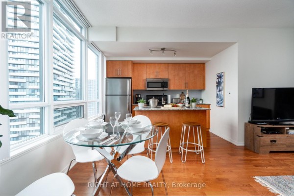Dining area with glass table and white chairs, open to kitchen with wood cabinets and stainless steel appliances. - 3404 - 55 Bremner Boulevard, Toronto