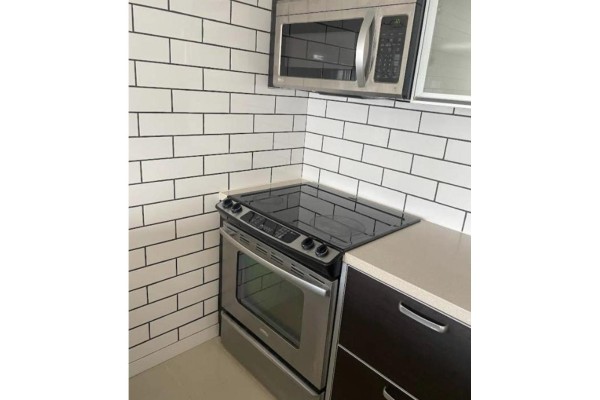 Close-up of a stainless steel stove with a glass top and a white subway tile backsplash. - 3404 13688 100 Ave, Surrey