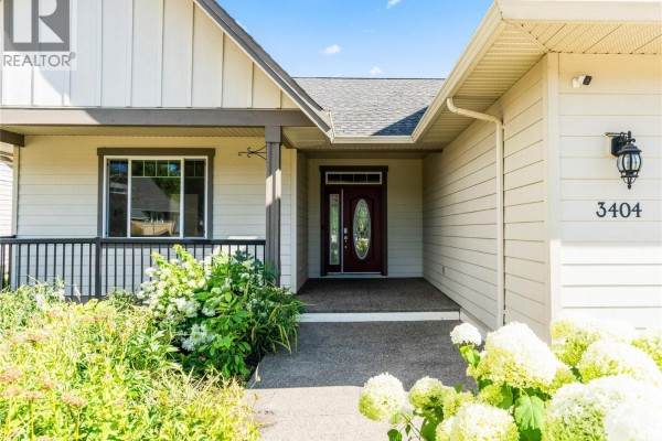 Close-up of a beige house entrance with a burgundy door and lush greenery. - 3404 Mckechnie Drive, Armstrong
