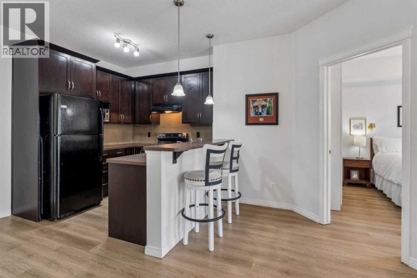 Kitchen with dark wood cabinets, black appliances, and a breakfast bar with stools. - 3407, 10 Country Village Park Ne, Calgary