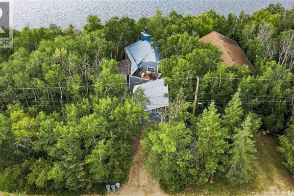 Aerial view of houses nestled among trees, with a gravel road and a wide body of water in the distance. - 3409 East Nickorick Beach, Wakaw Lake