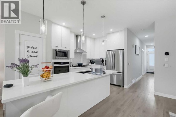 Modern white kitchen with a large island, stainless steel appliances, and pendant lighting. - 341 Calhoun Common Ne, Calgary