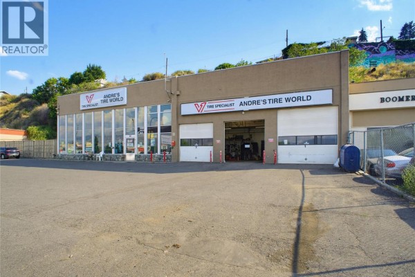 View of commercial building's garage bay doors and signage. Vehicles and parked in lot. - 341 Victoria Street W, Kamloops