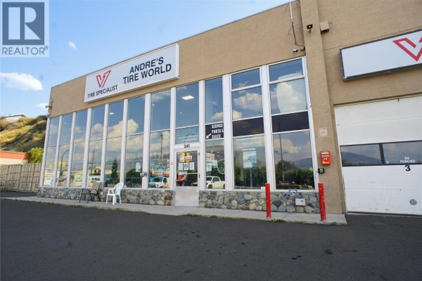 Close-up of commercial building's storefront with large windows displaying tires and products. Stone base visible. - 341 Victoria Street W, Kamloops