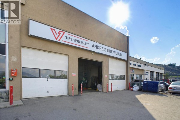 Two white garage bay doors with one open showing interior equipment. Andre's Tire World signage above. - 341 Victoria Street W, Kamloops