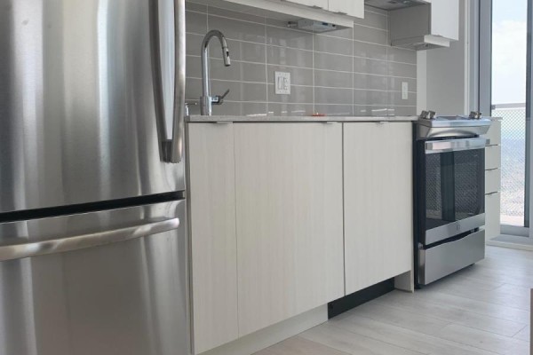 A partial view of a kitchen with stainless steel refrigerator, light wood cabinets, and a window view. - 3410 - 4065 Confederation Parkway, Mississauga