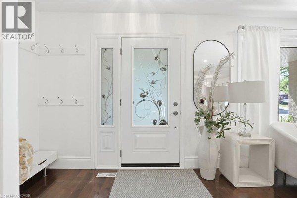 Interior entryway with a white front door, frosted glass sidelights, a tall mirror, and a modern end table. - 3411 Lansdown Drive, Burlington