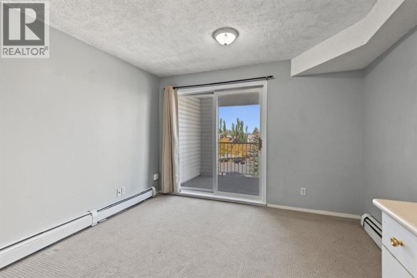 Bedroom with beige carpet, sliding glass door to balcony, and beige dresser. - 3415, 1620 70 Street Se, Calgary
