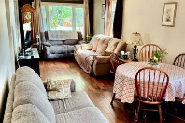 Living area with multiple couches, a dining table, chairs, a grandfather clock, and hardwood floors. - 342 Barton Street, Hamilton