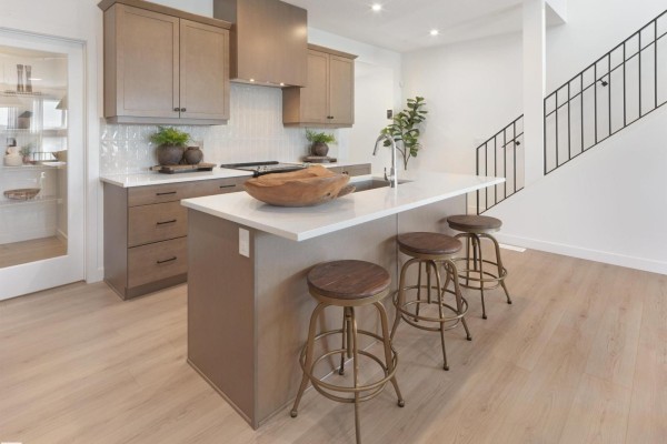 Kitchen island with white quartz countertop and three bar stools facing a stainless steel sink. - 342 Stiles Wy, Leduc